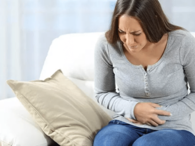 young woman sitting on her couch with stomach pain
